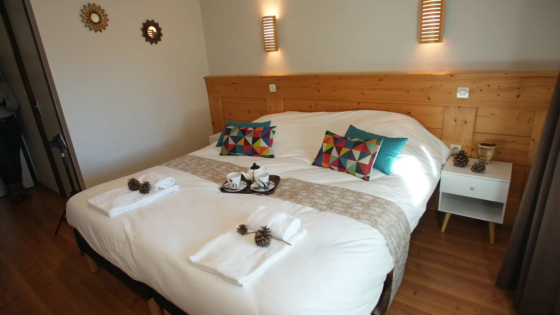 Lit double avec coussins, serviettes, plateau avec tasses et théière posés au centre. Tête de lit en bois
