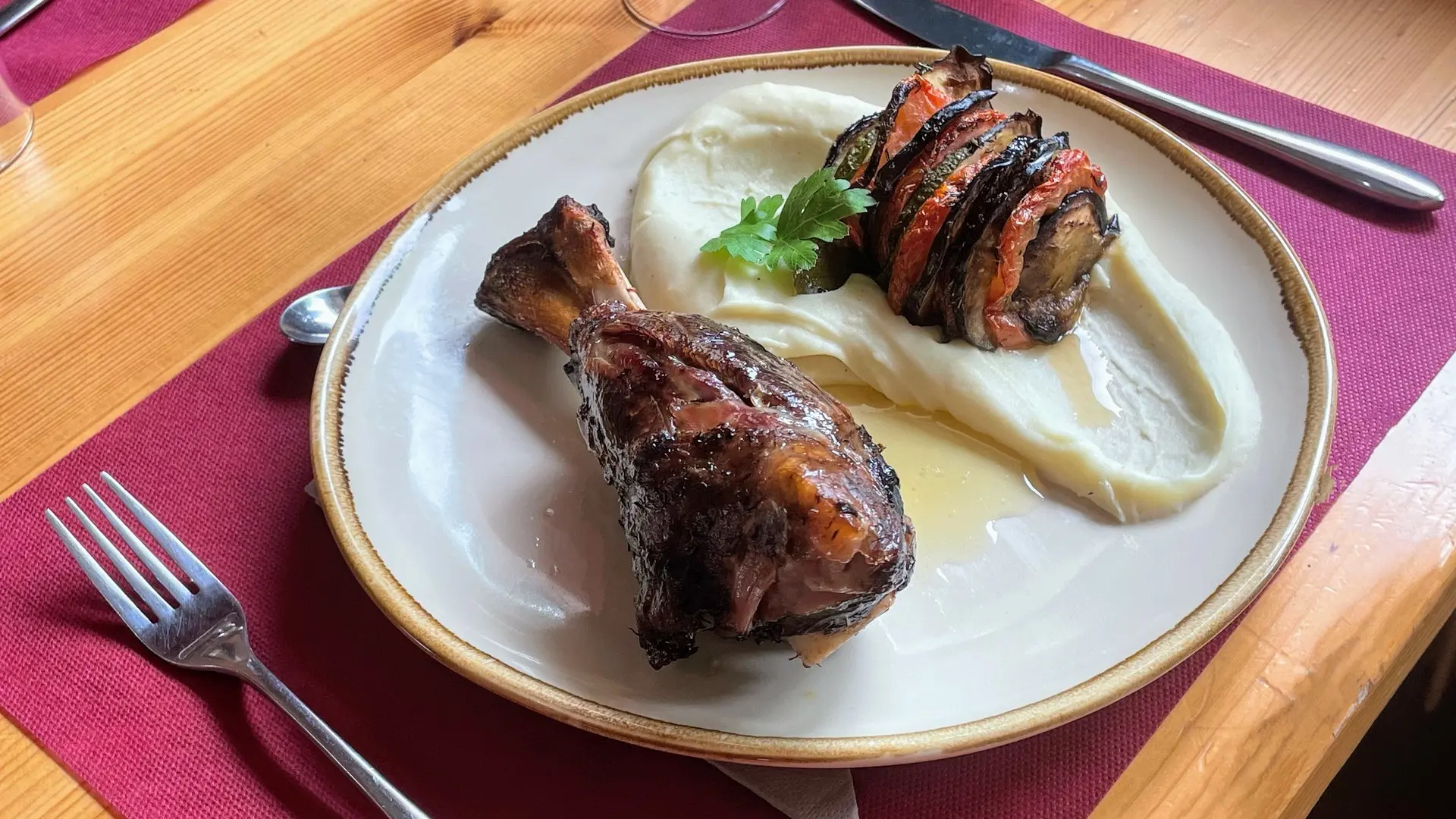Souris d’agneau servie dans une assiette ronde, sur un set de table bordeaux.