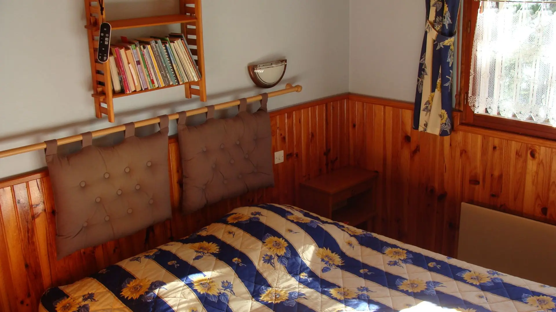 Chambre à coucher lumineuse avec lit double, ameublement bois et lambris, fenêtre et rideaux