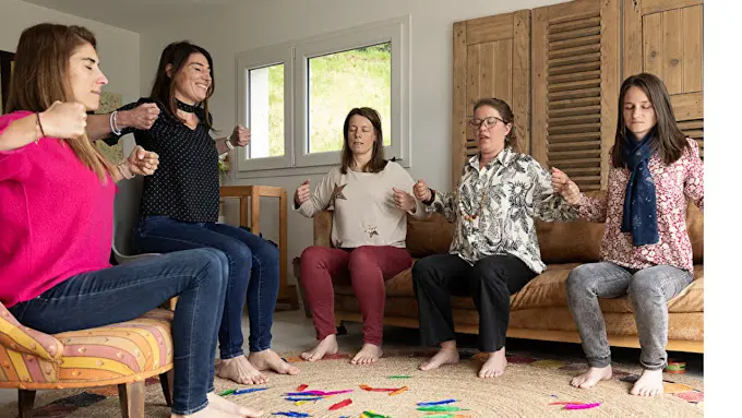 5 femmes pratiquant un atelier de sophrologie avec des plumes colorées sur le sol.