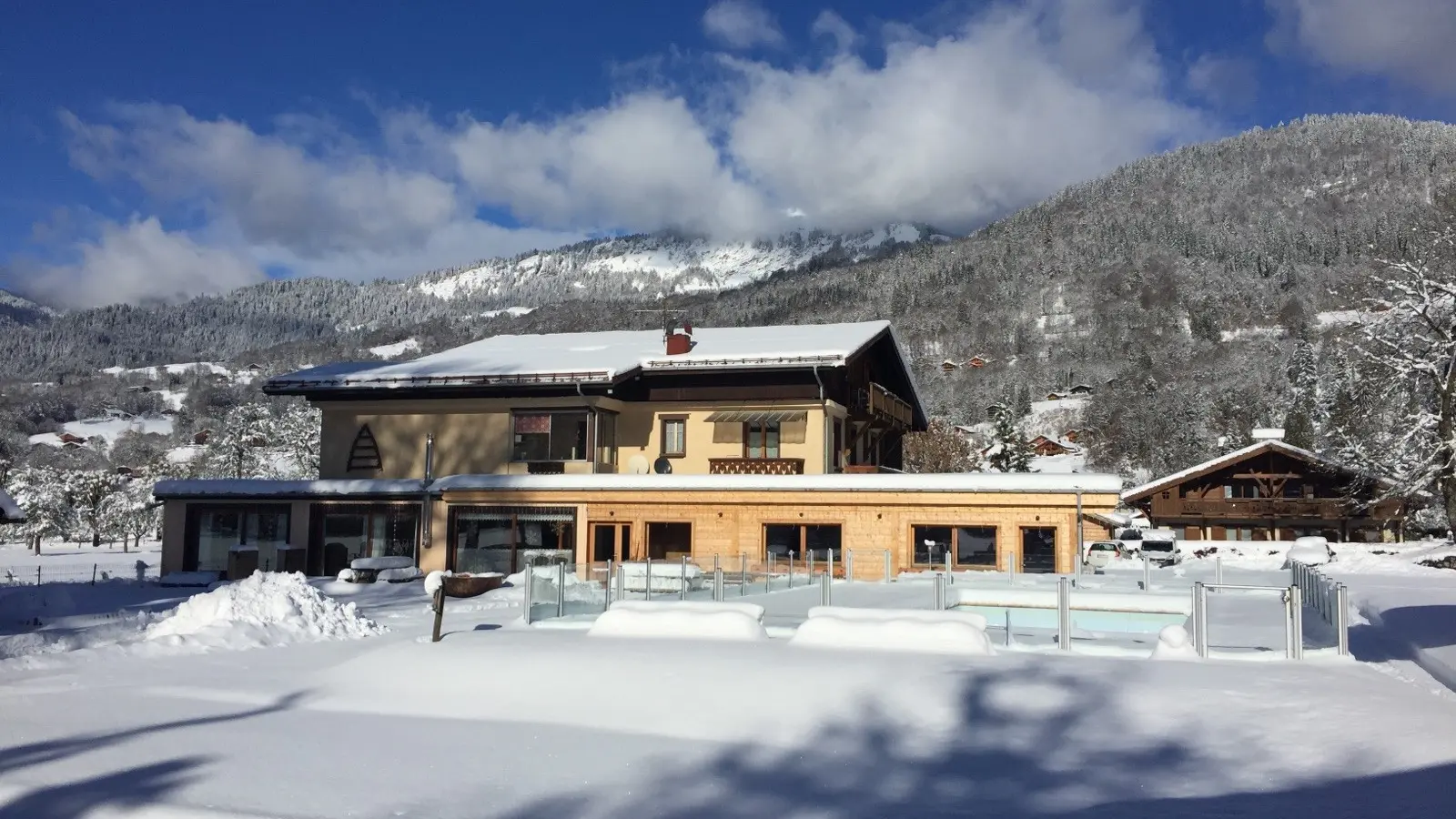 Vue de la façade sud de l'hébergement et sur la piscine recouverte par la neige depuis le jardin