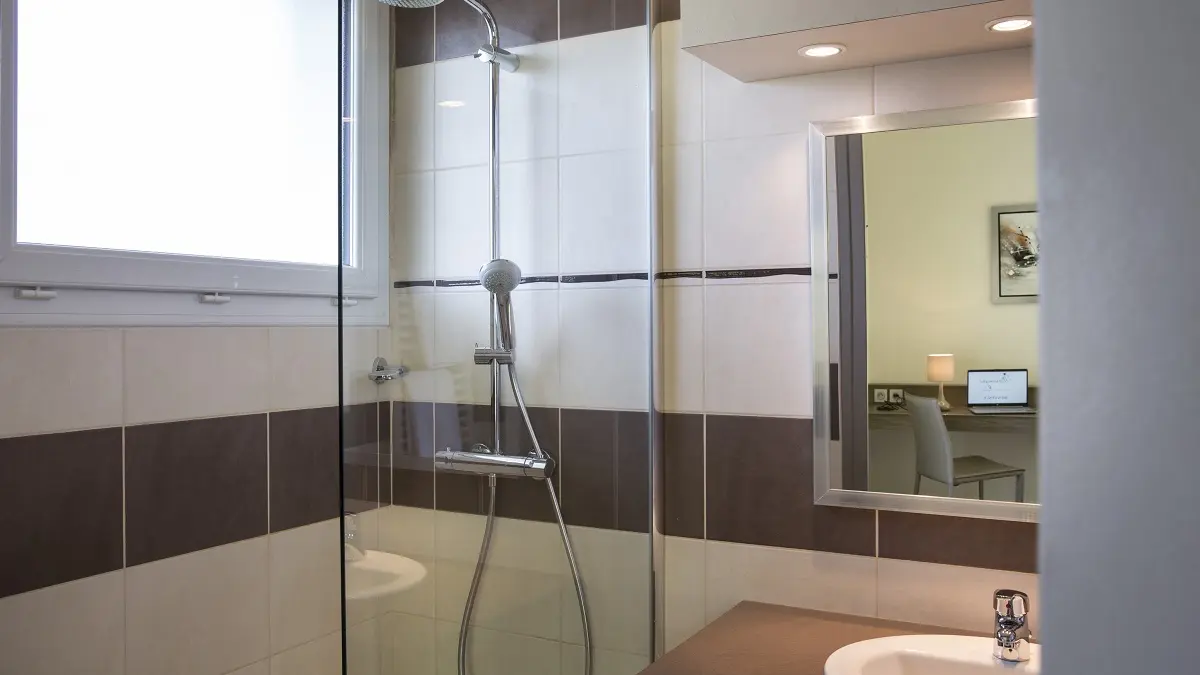 Cette salle de bain, baignée de lumière naturelle, présente un design contemporain avec des carreaux de céramique aux motifs géométriques et une paroi de douche en verre transparent, créant un espace à la fois fonctionnel et esthétique.