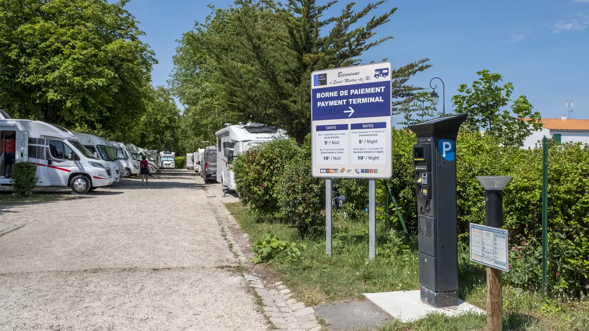 Vue d'ensemble avec des camping cars stationnés, le panneau de tarification et un horodateur.