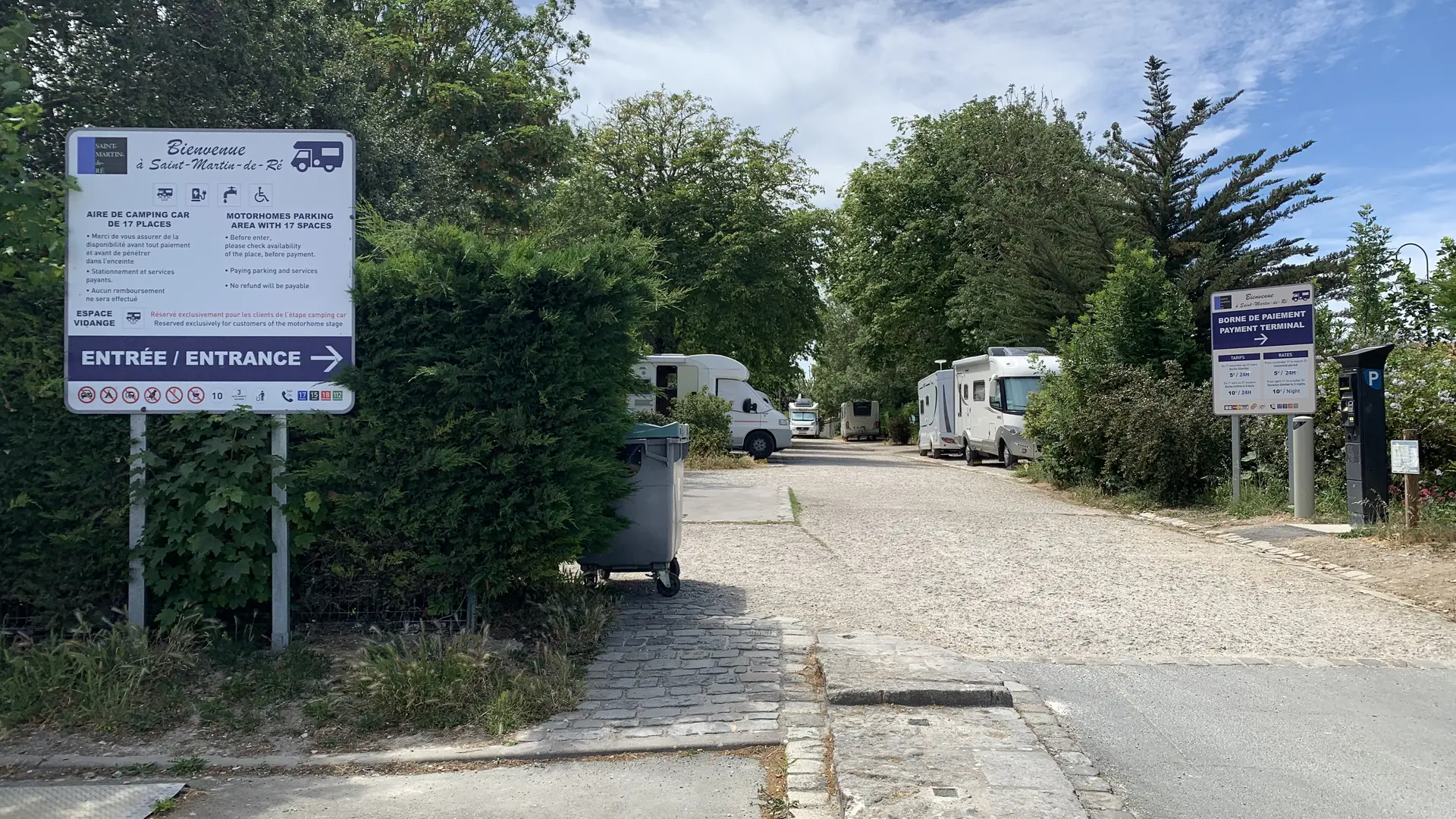 Vue d'ensemble avec des camping cars stationnés, le panneau de tarification et un horodateur.