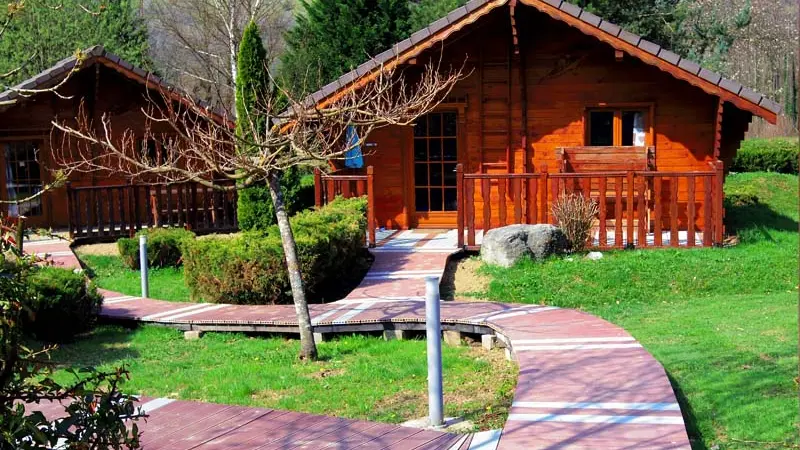 Deux chalets en bois sont adossés à un chemin sinueux bordé d'une pelouse verdoyante.