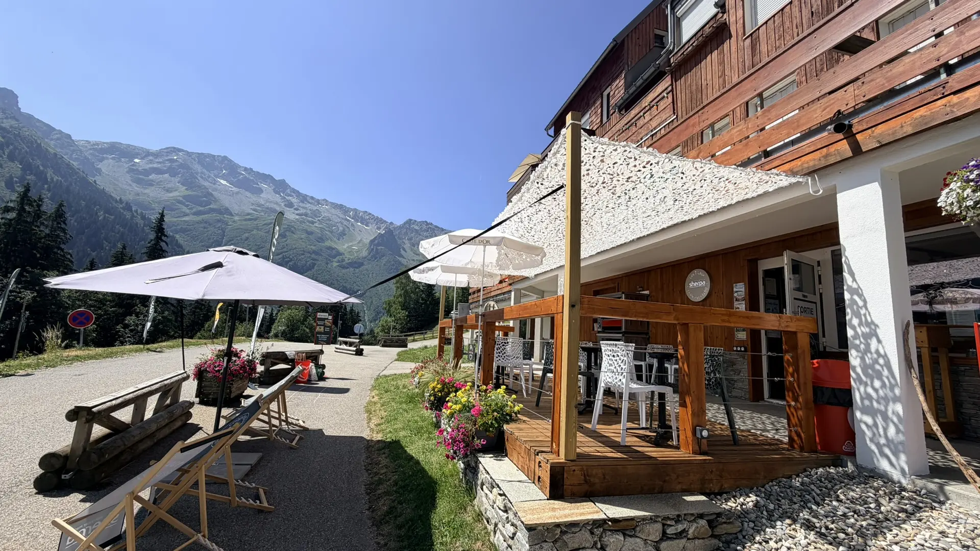 Devanture du Sherpa au Pleynet l'été des chaises longues et parasols et une vue sur le massif de Belledonne