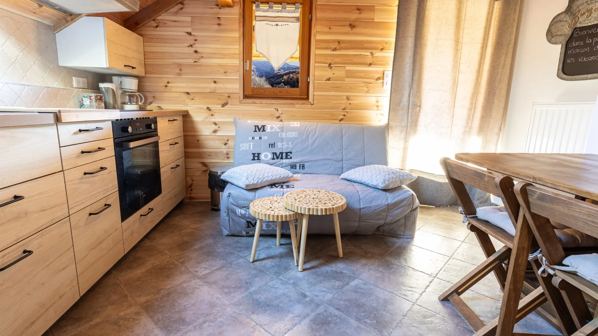 Séjour lumineux avec coin cuisine, TV, table à manger, canapé, ameublement bois, carrelage au sol, porte-fenêtre