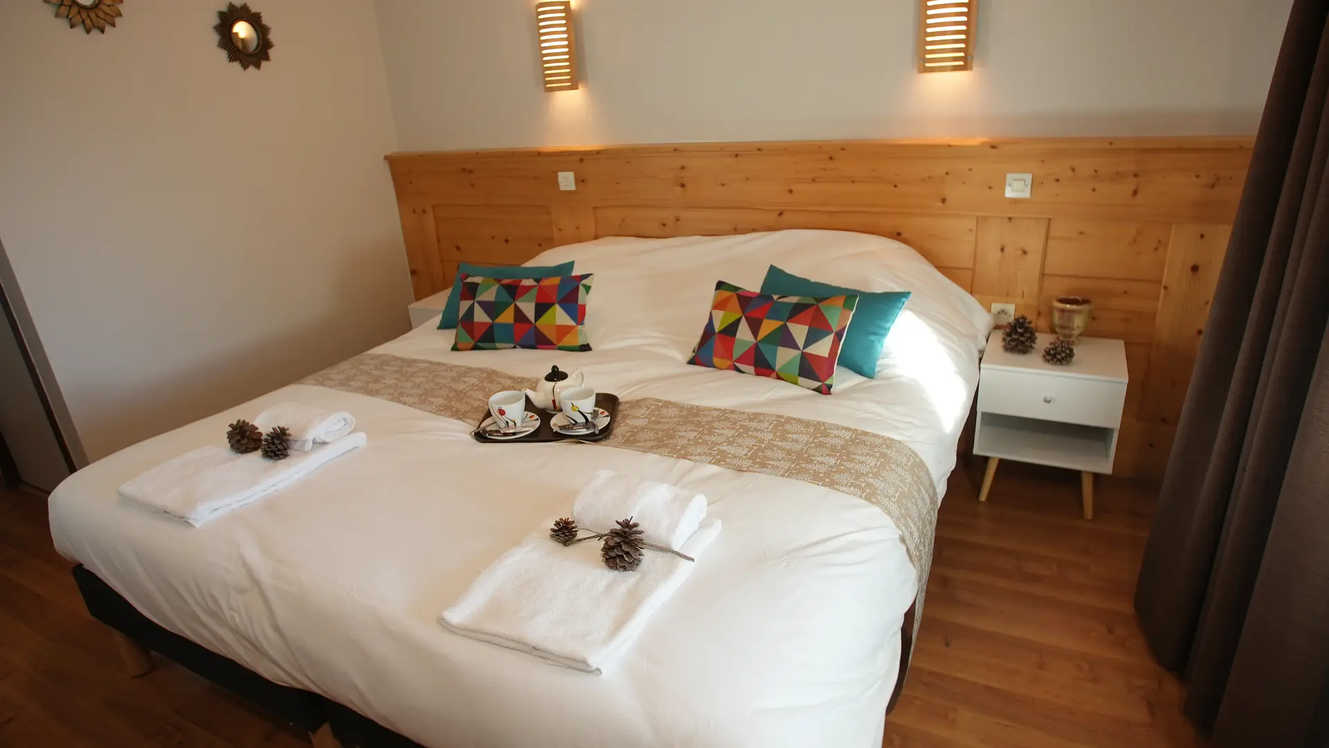 Lit double avec coussins, serviettes, plateau avec tasses et théière posés au centre. Tête de lit en bois