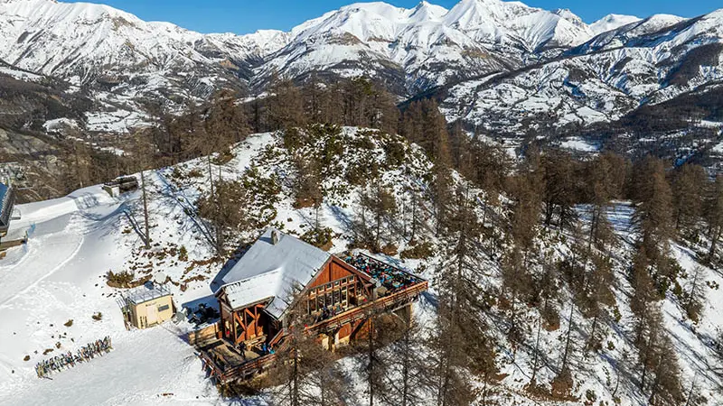 Vue du restaurant d'altitude en drone, chalet en bois et pierre au milieu des montagnes enneigées, terrasse en bois