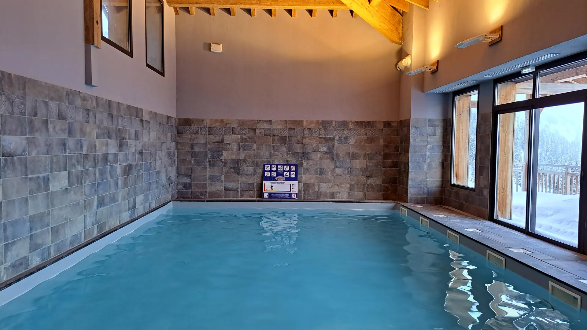 A bright indoor swimming pool with a wooden frame, offering views of the outdoors.