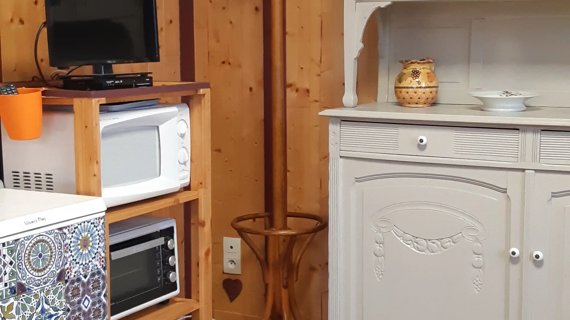 C'est une cuisine fonctionnelle, équipée d'un réfrigérateur, d’un buffet d'un meuble en bois avec un four et d'un micro-ondes surmonté d’un écran de télévision.