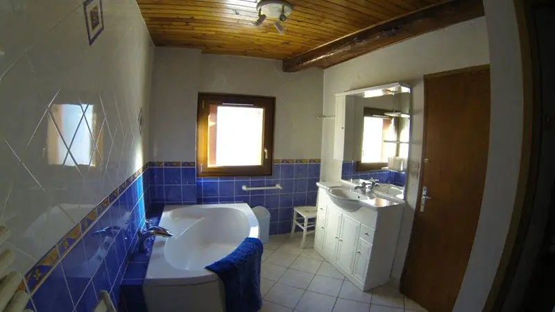 Bright, tiled bathroom with bathtub, wooden furniture, and window