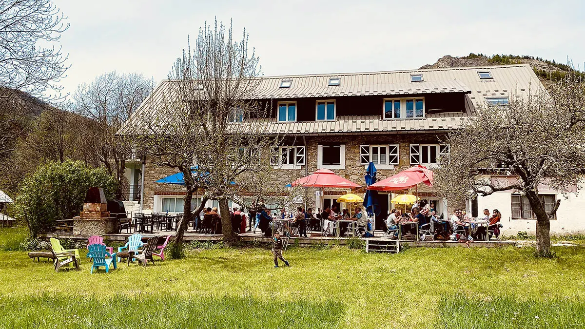 View of the restaurant in summer, a large 3-story stone building, outdoor terrace with tables and chairs, in a meadow setting