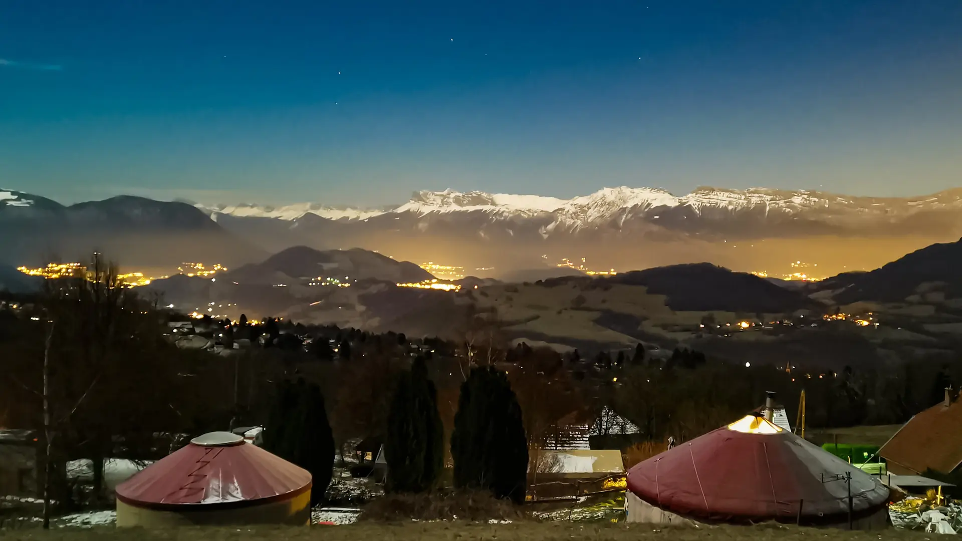 Deux yourtes rouges avec leurs terrasses au crépuscule avec le Vercors au fond.