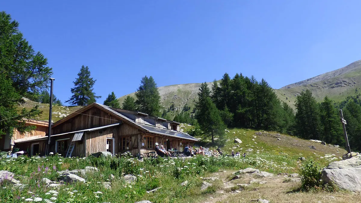 Vue du refuge-restaurant, maison en bois au milieu de la végétation, terrasse, tables et chaises