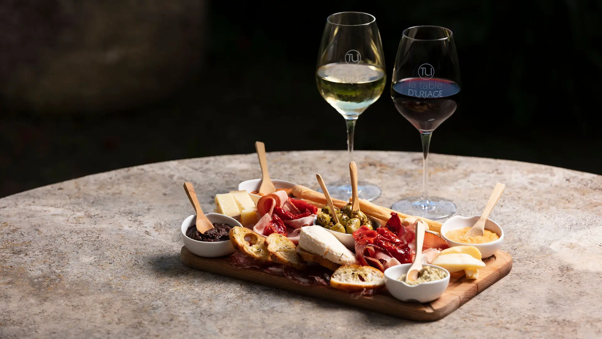 Cette image présente une planche de charcuterie et de fromages, ainsi que deux verres à vin.