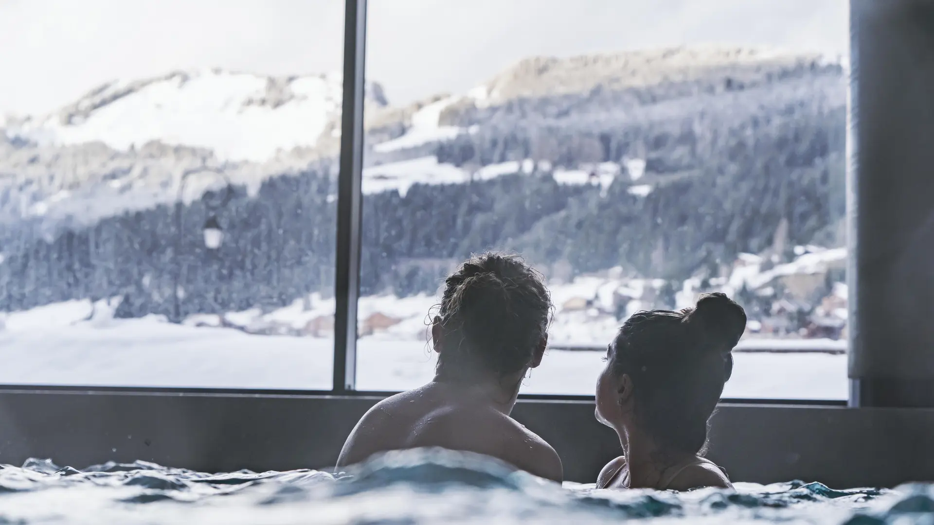 Couple qui admire la vue du village enneigé depuis le bassin du spa Océane