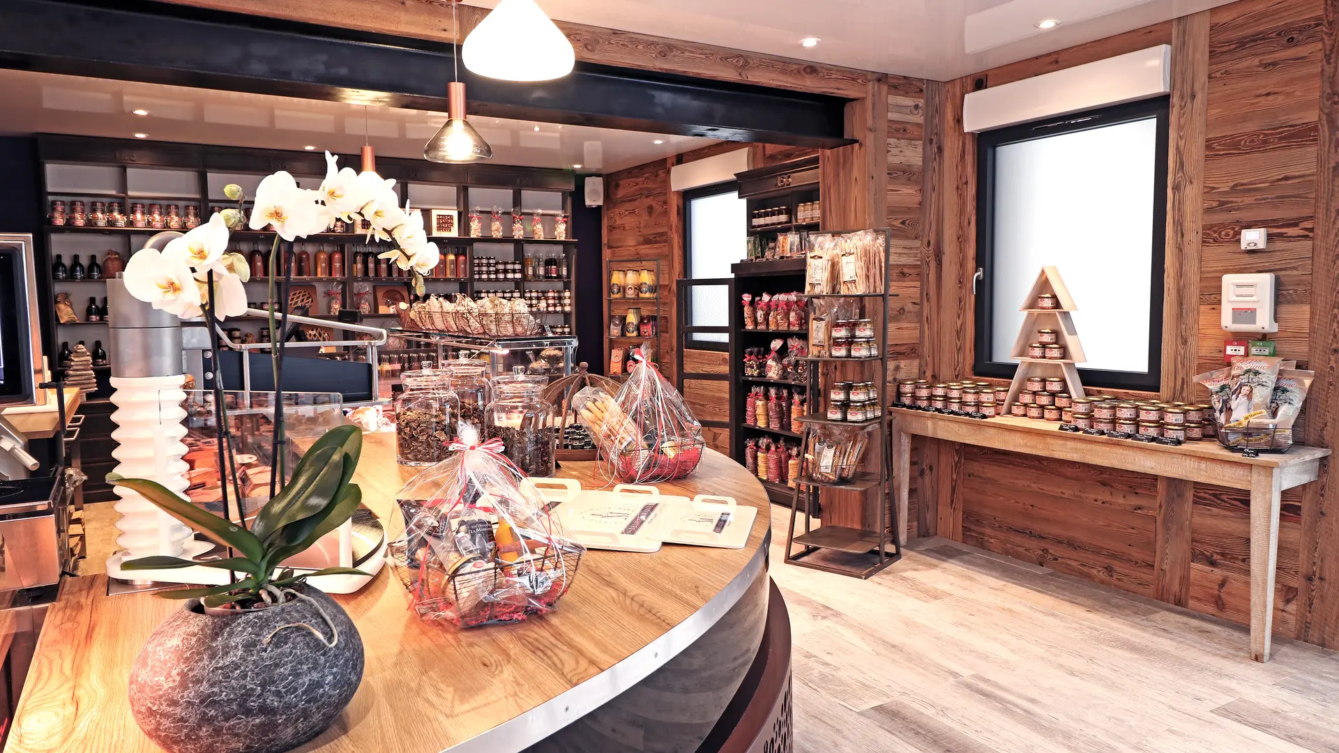 Comptoir d'accueil partie droite, côté épicerie fine, avec une orchidée posée dessus au premier plan et des étagères avec des produits fins dans le fond.