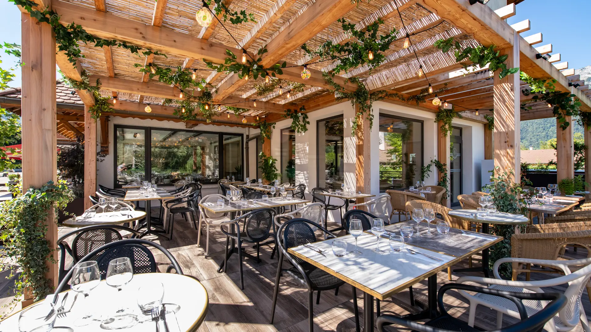 terrasse avec tables dressées sous pergolas en bois et végétaux