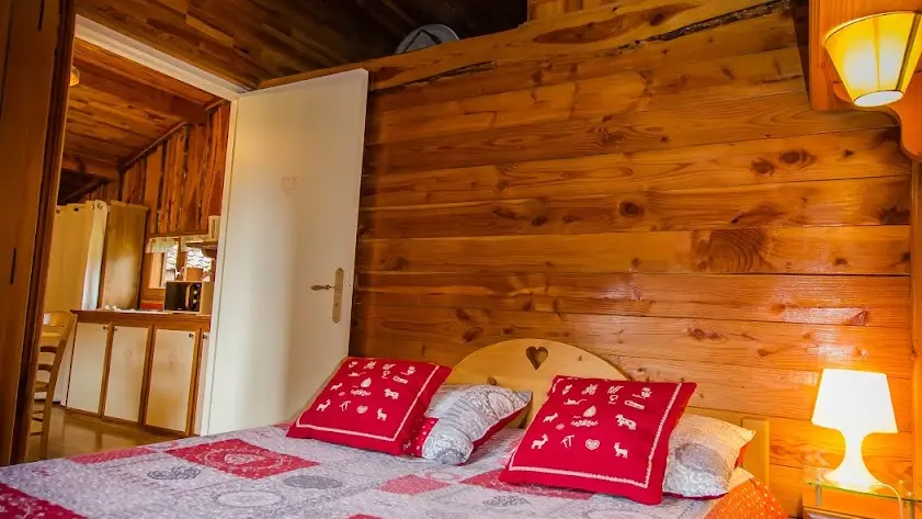 Le chalet présente une chambre à coucher spacieuse avec un lit double, des murs et un plafond en bois, créant une ambiance chaleureuse et montagnarde.