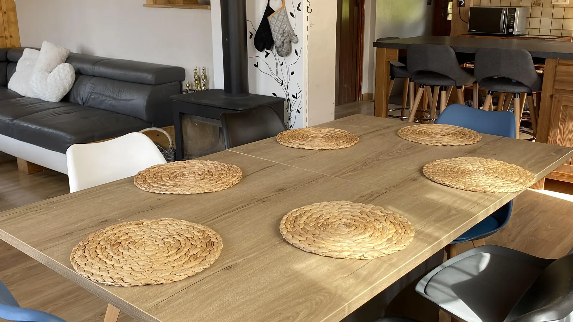 Salle à manger avec salon à côté, poêle à bois, cuisine en arrière plan
