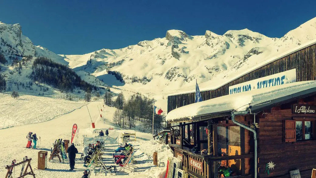 Vue de côté du restaurant d'altitude, bâtiment en bois, terrasse extérieure avec chaises longues le long des pistes enneigées, panneau Altiplano - Altitude. Montagnes en arrière-plan