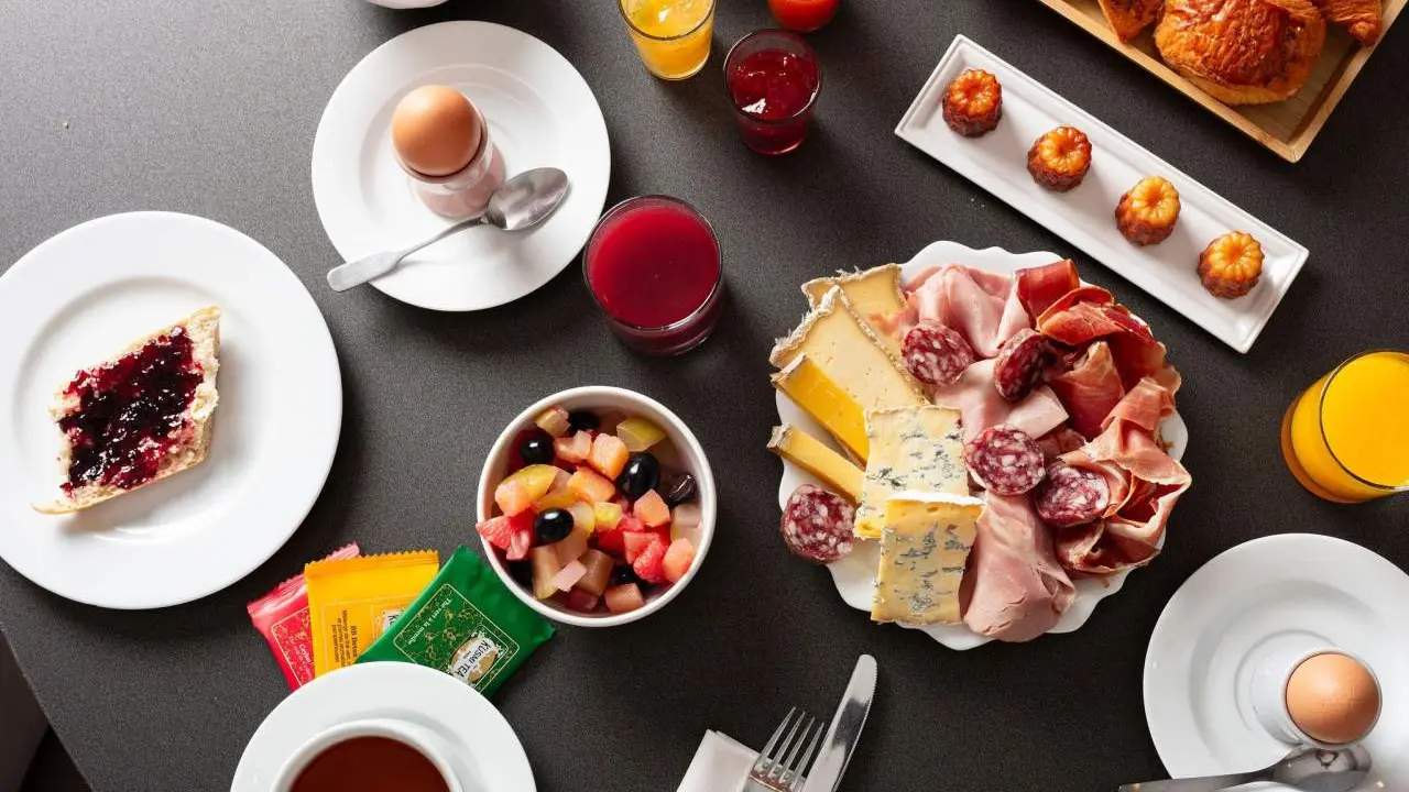 Ce brunch offre une grande variété de plats comme des viennoiseries, du pain frais avec de la confiture, une assiette de charcuterie et de fromages avec du jambon, du saucisson et différents fromages.