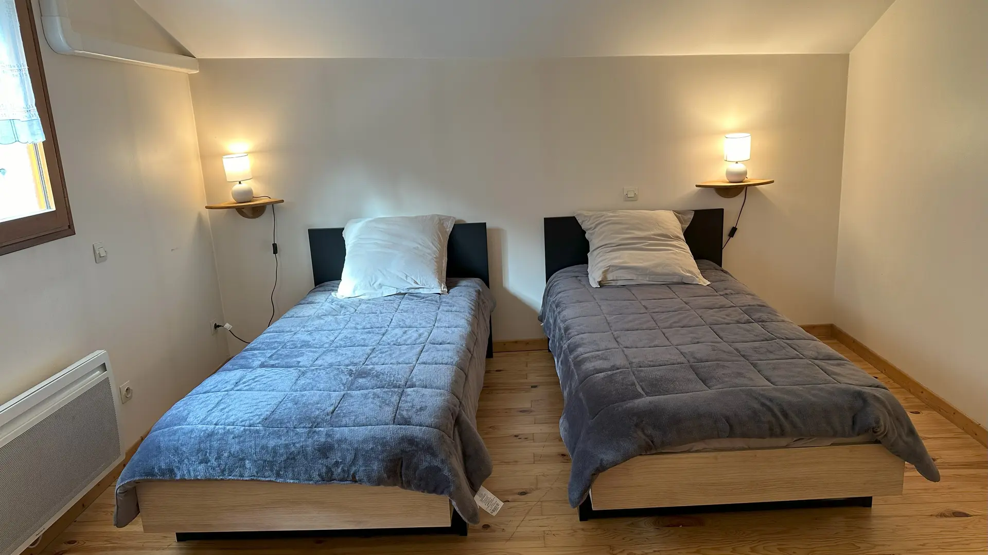 Cette chambre mansardée est lumineuse. En entrant dans la chambre, vous avez les deux lits simples face à vous, placés côte à côte. La fenêtre est située sur le mur de gauche. Les lampes de chevet sont sur les tables de nuit, de chaque côté des lits.