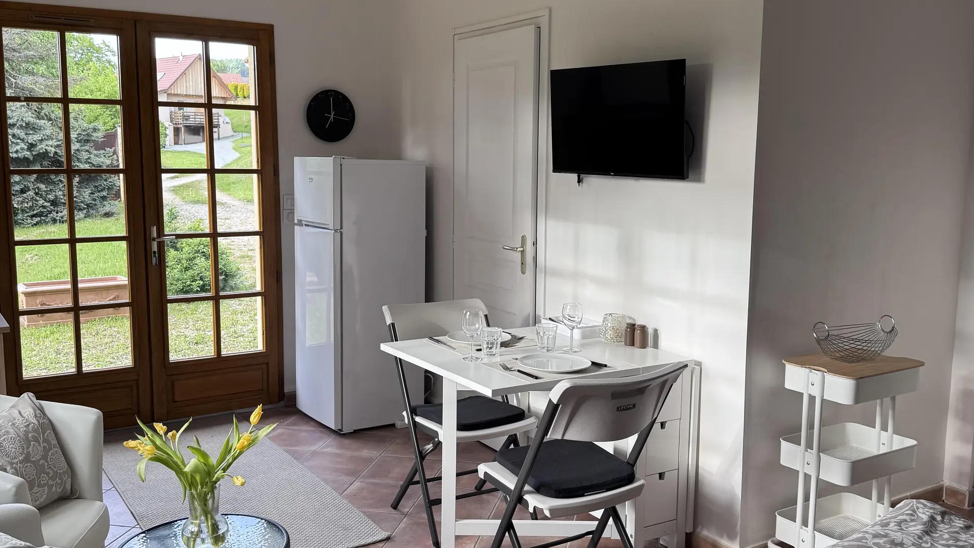 Espace ouvert aux murs clairs, combinant un coin repas et un coin salon, lumineux grâce à une grande porte-fenêtre donnant sur un jardin.