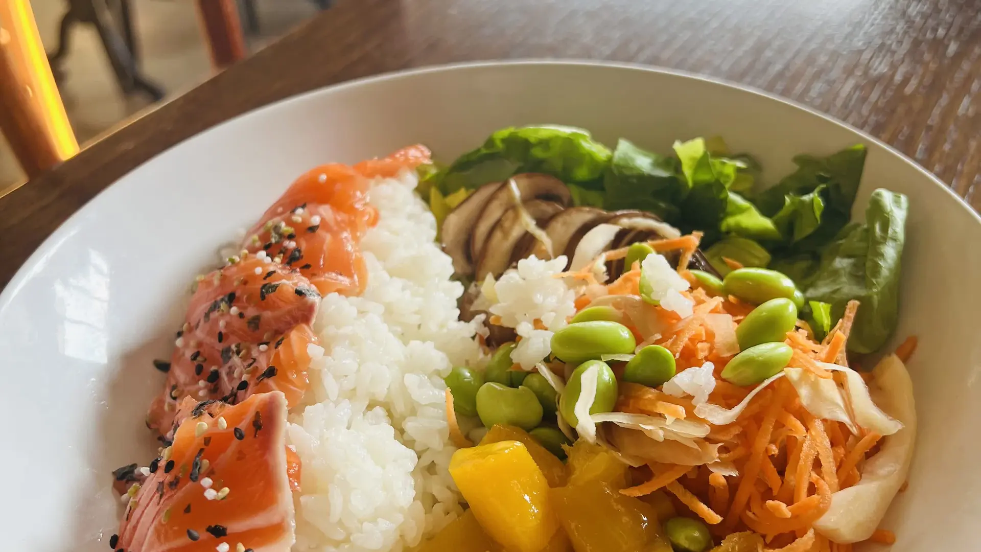 Bol coloré de poké au saumon, riz, mangue et légumes croquants.