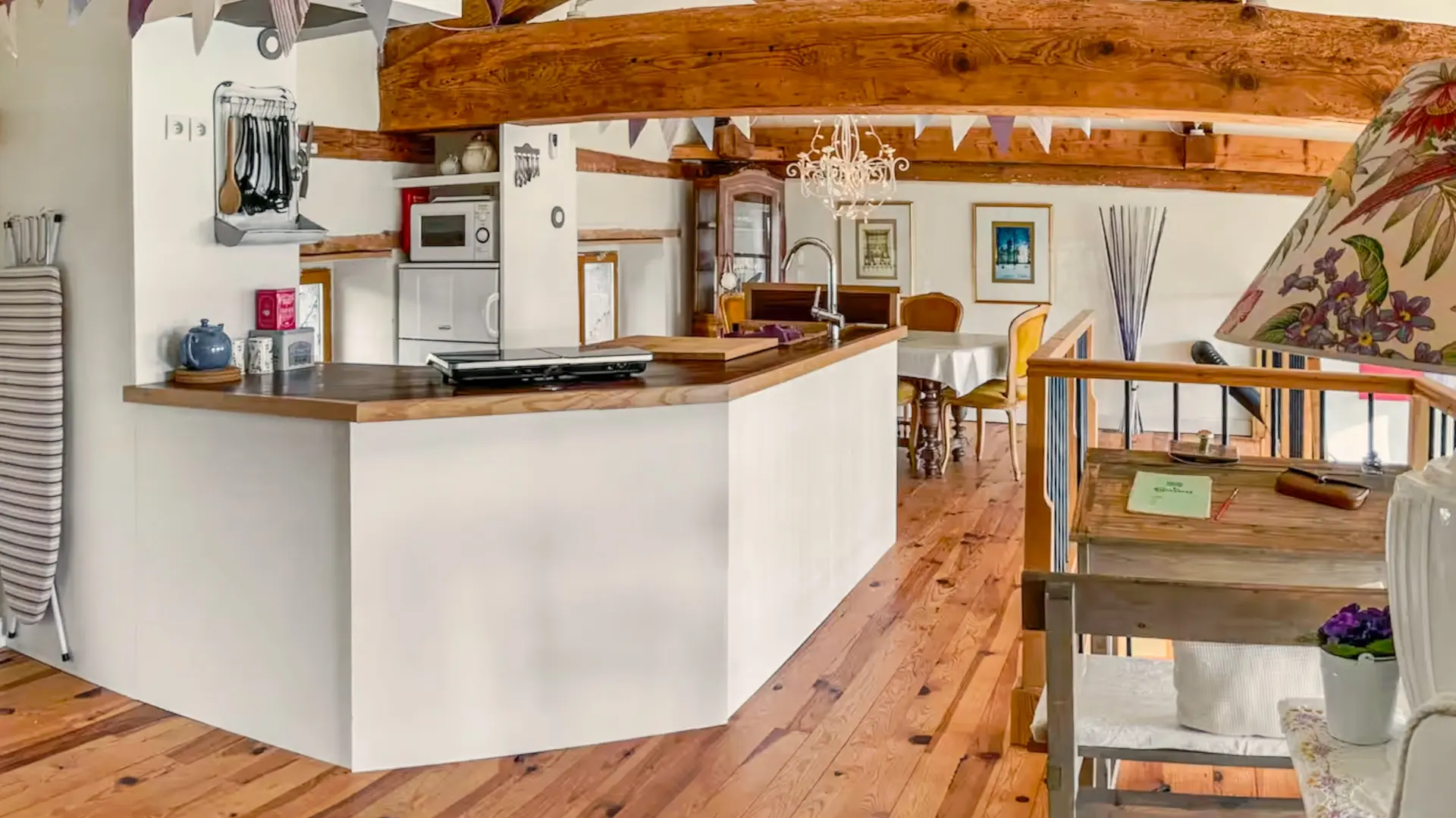 La cuisine se trouve entre la salle à manger et le salon de la mezzanine. Une petite cuisine américaine avec le nécessaire pour cuisiner. Le bar en bois est de forme octogonale ouvert avec un évier, une table à induction et sa bouilloire et contre le mur, une machine à café. On aperçoit des ustensiles de cuisine accroché à un support ancien détourné. A droite, une niche avec une étagère comprenant trois théières. En dessous, il y a un micro-onde et une réfrigérateur (frigo et une partie congélation). Au dessus de la fenêtre, on trouve un support magnétique pour ranger les couteaux de cuisine. La luminosité de la mezzanine est apportée par la lumière traversante venant des fenêtres.