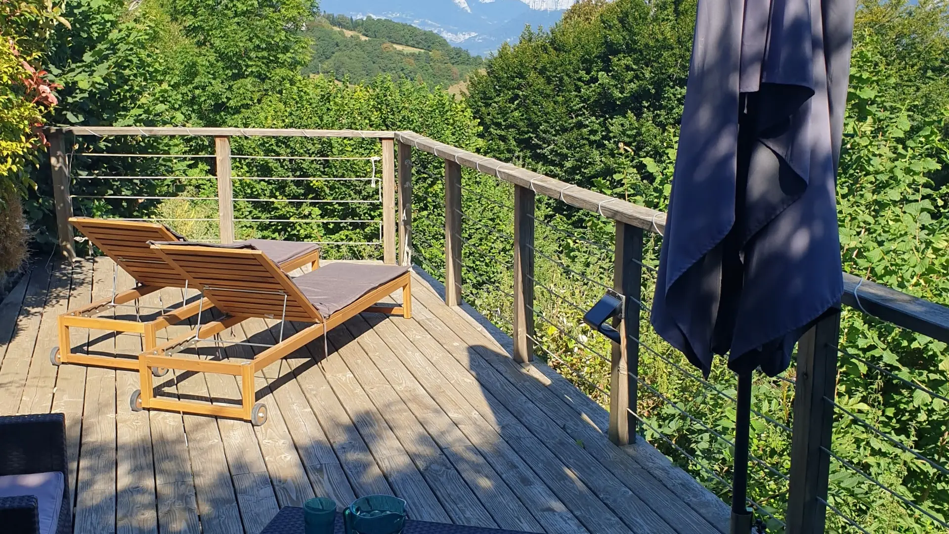 Vue sur la nature depuis une large terrasse aménagée cote ensoleillé avec deux transats et un coin assis