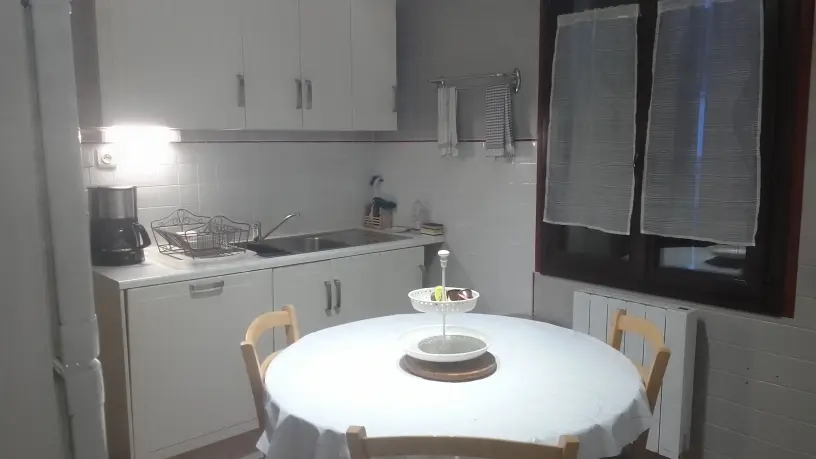 Pièce aménagée en cuisine, comprenant un espace repas avec une table ronde et des chaises en bois clair. Le sol est recouvert d'un parquet clair. Une fenêtre apporte de la lumière naturelle à la pièce.