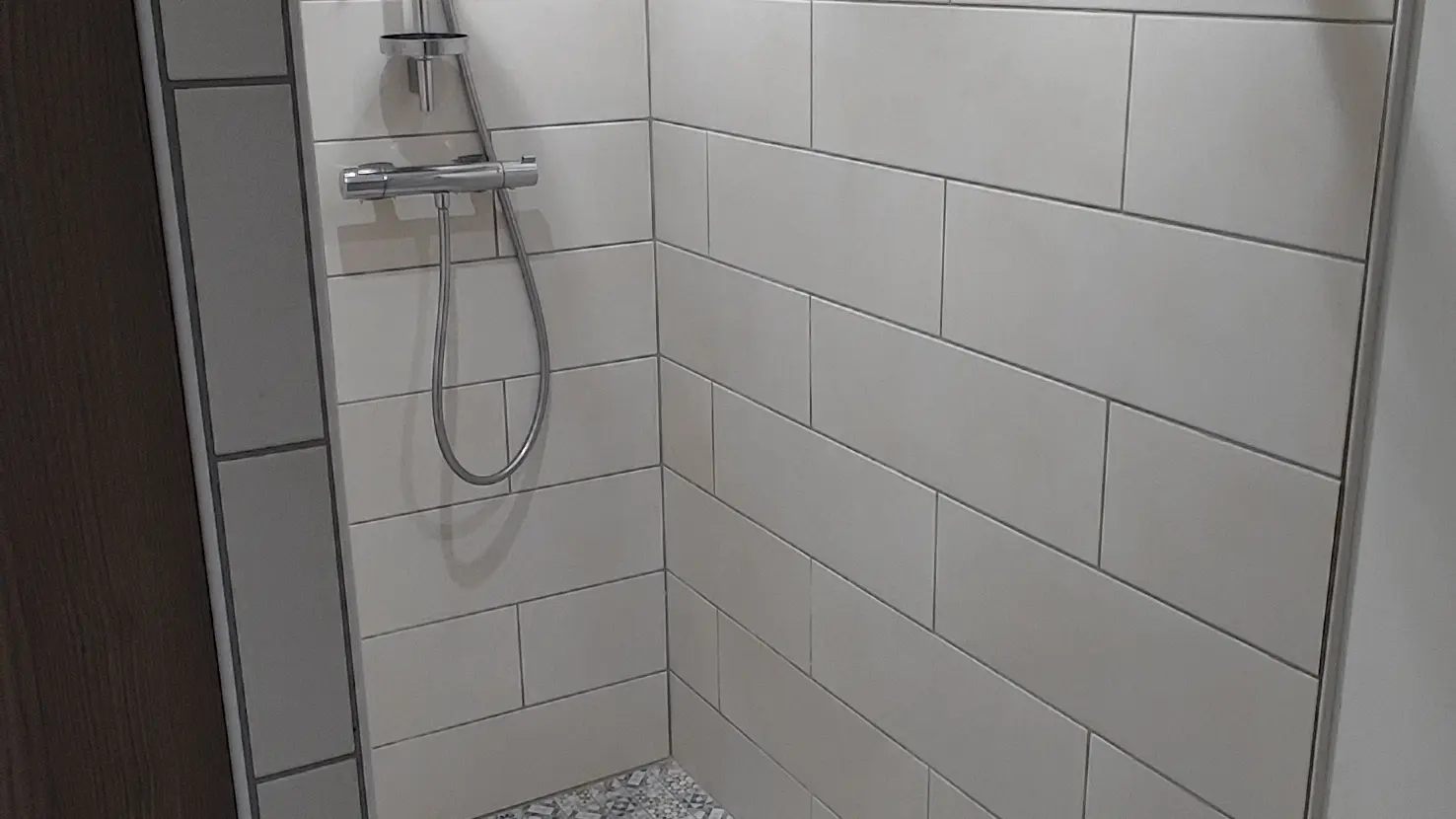 Cette pièce d'eau possède une douche moderne dotée de parois vitrées transparentes, d'un receveur de douche blanc bas et d'un pommeau de douche fixé sur un mur aux tons clairs.