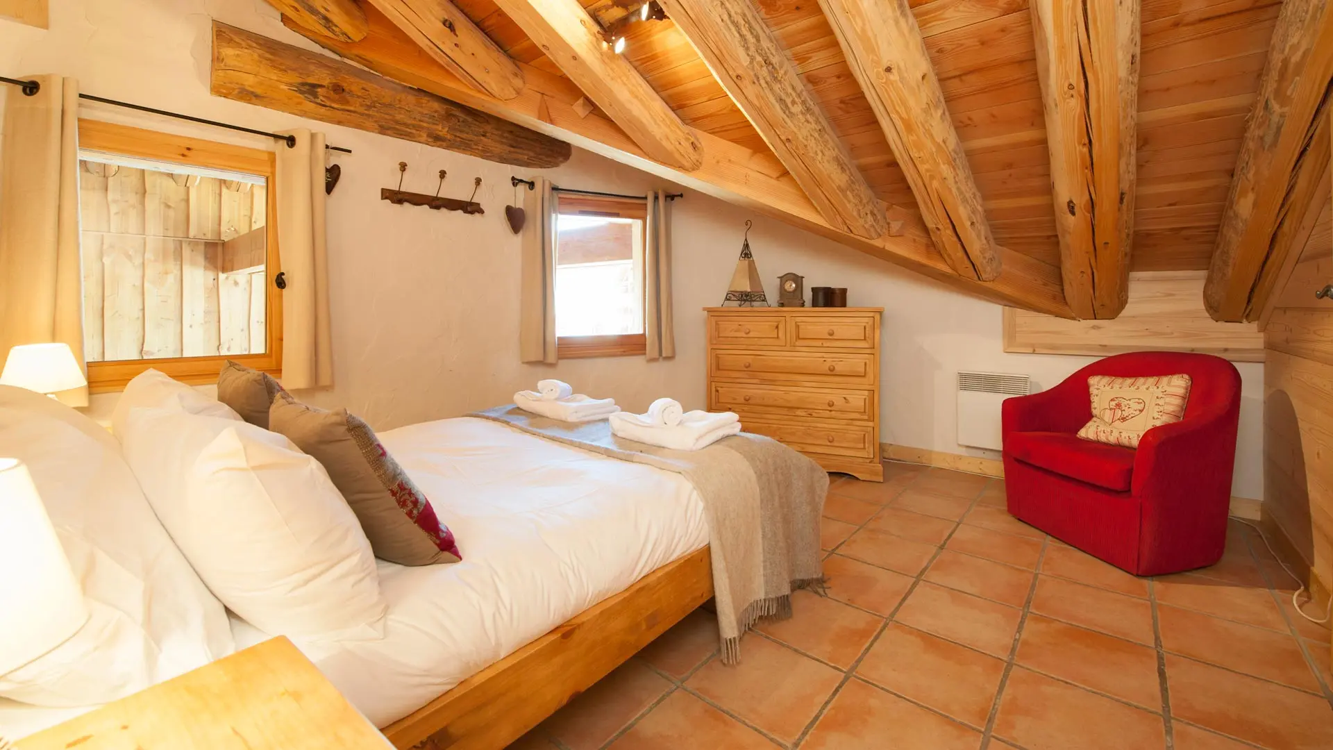 Chambre double avec lit en 140 cm, fauteuil, plafond mansardé avec poutres apparentes, deux fenêtres, patères, commodes avec 5 tiroirs, radiateur électrique.
