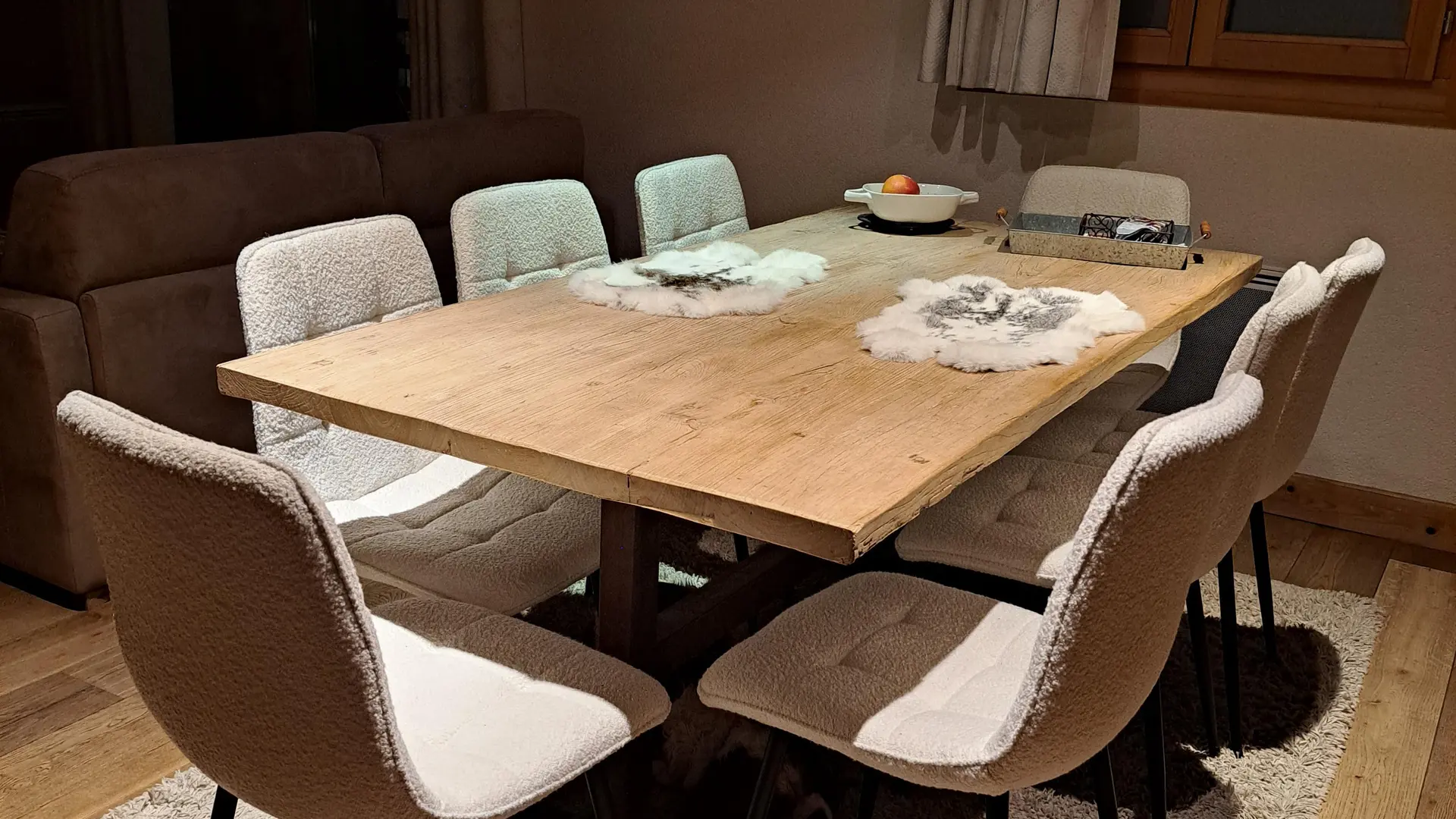 A cozy dining room with a light wooden table surrounded by white boucle-effect chairs.