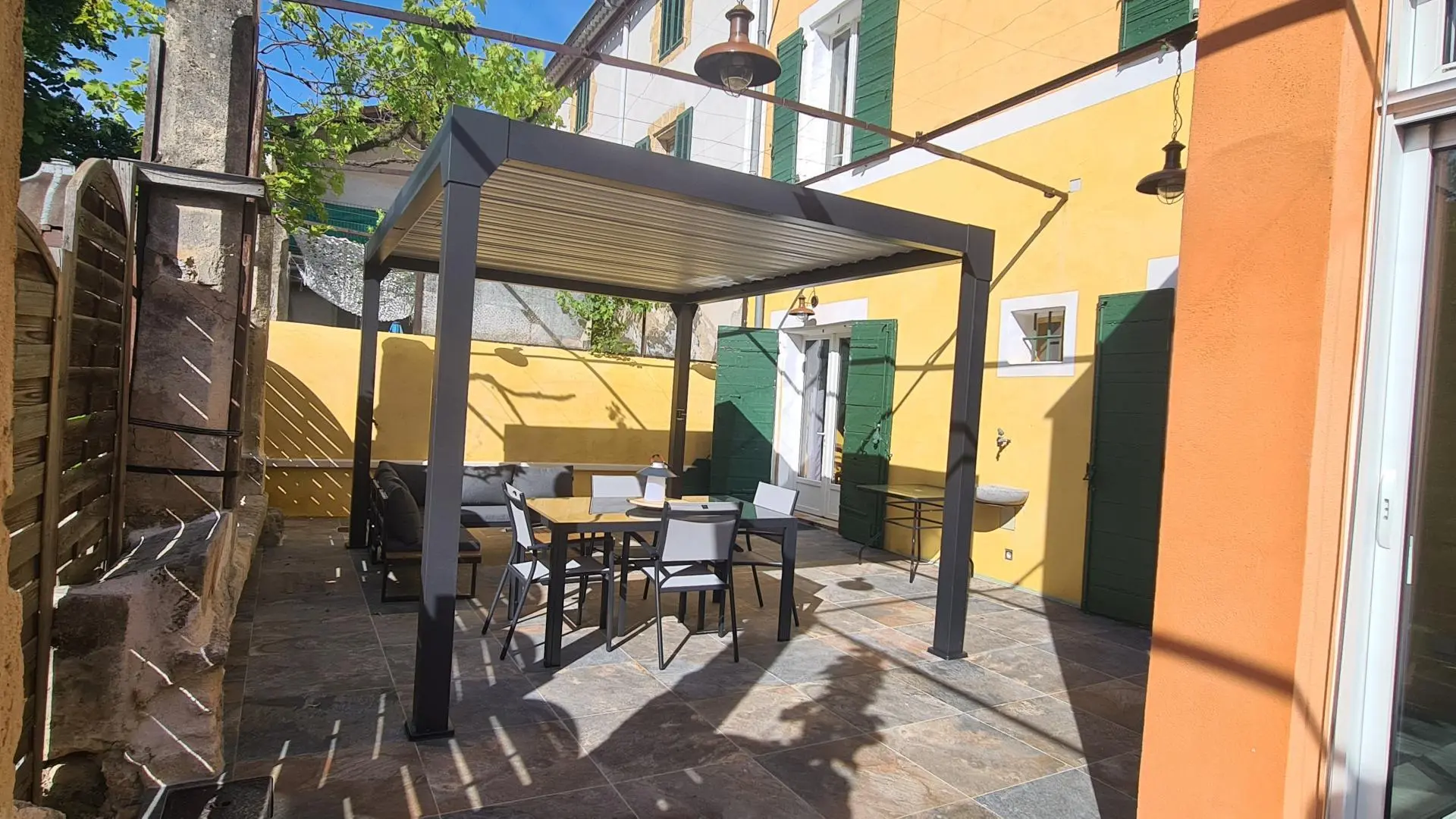 Cour privative du gîte. Pergola avec salon d'angle et table.