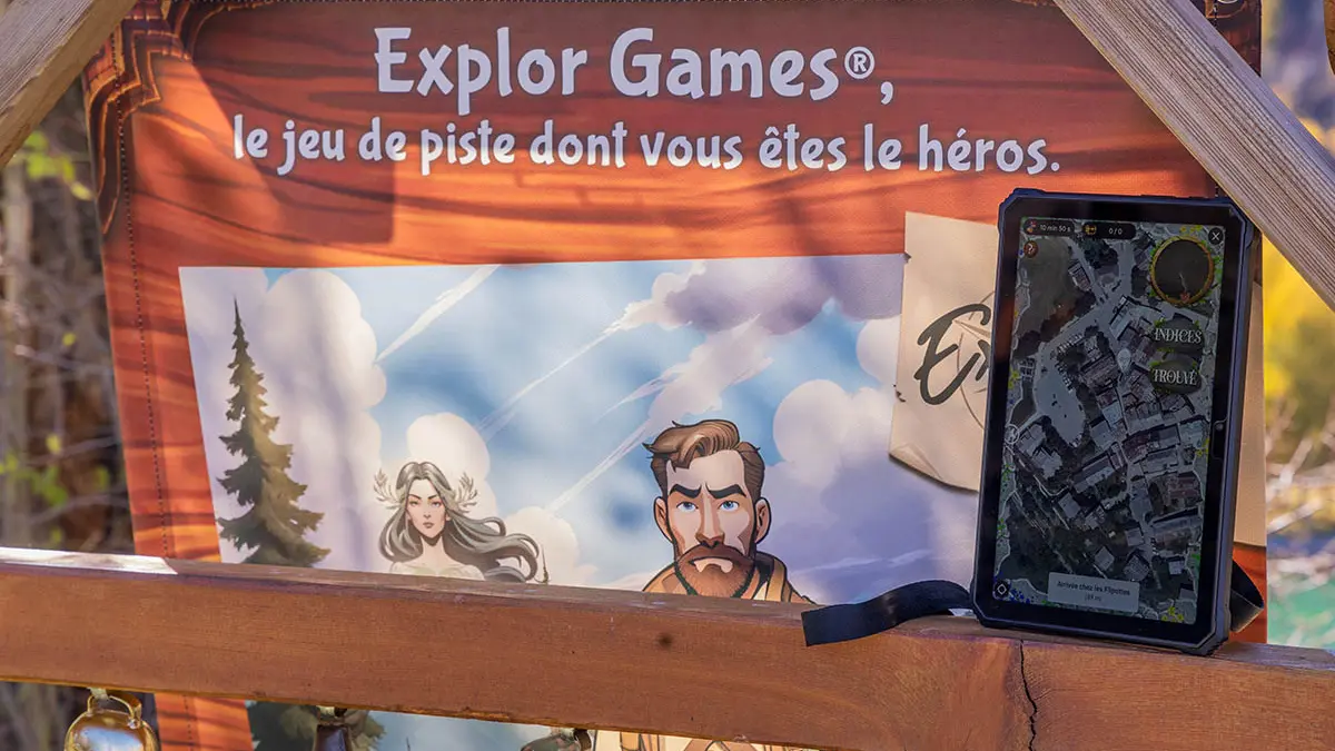 Panneau au départ du jeu Explor Games, inscription : Explor Games : le jeu dont vous êtes le héros. Tablette du jeu posée sur le côté.