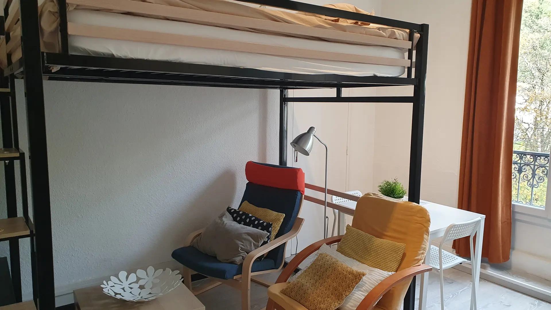 Ce studio est aménagé avec un lit mezzanine, deux fauteuils et une table et deux chaises à manger.