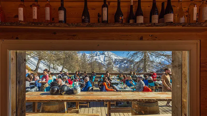 Terrasse du restaurant vue depuis l'intérieur, bois, tables et chaises, vue sur les montagnes enneigées en arrière-plan