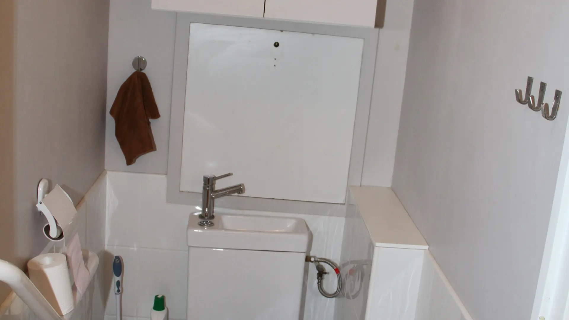 Les toilettes sont blanches avec une armoire blanche au-dessus et un lave-mains au-dessus de la cuvette.