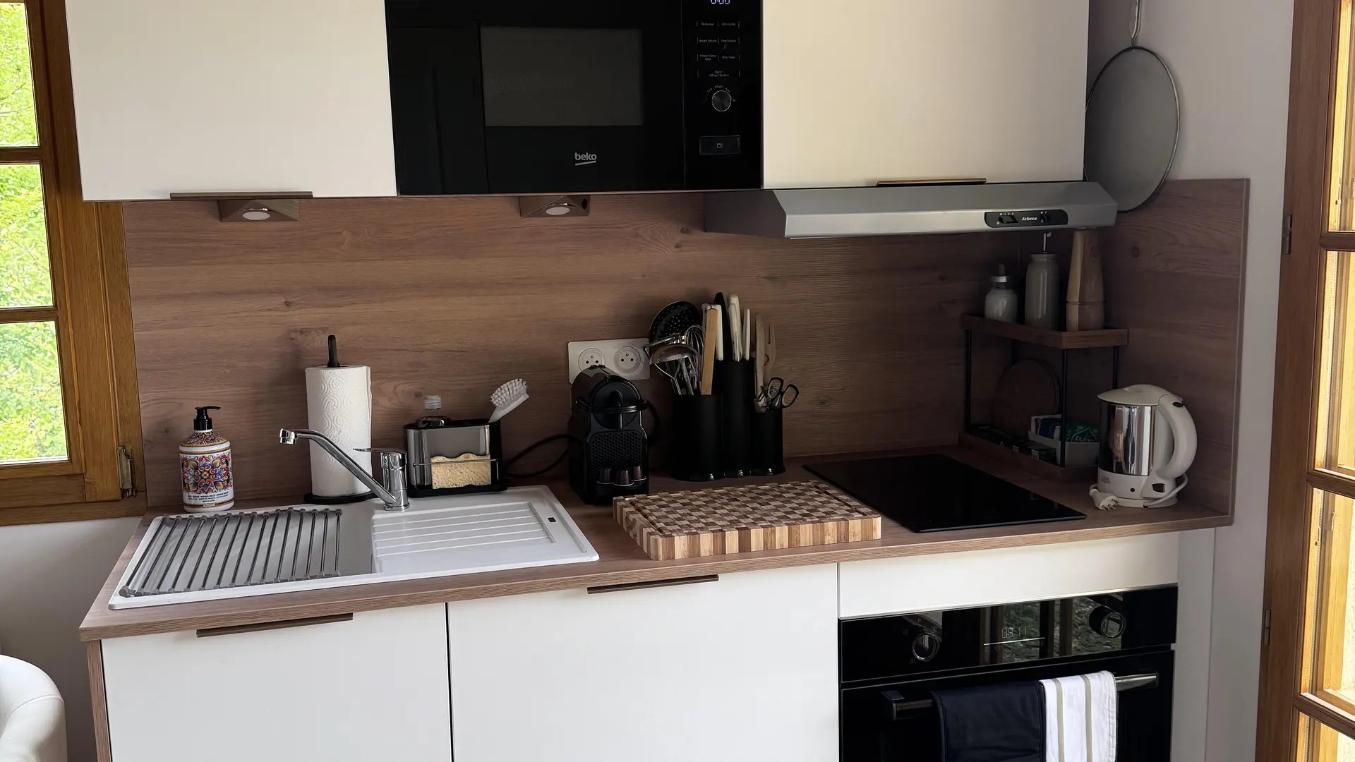 Kitchenette compacte avec placards blancs, plan de travail effet bois et appareils électroménagers noirs (micro-ondes, four)