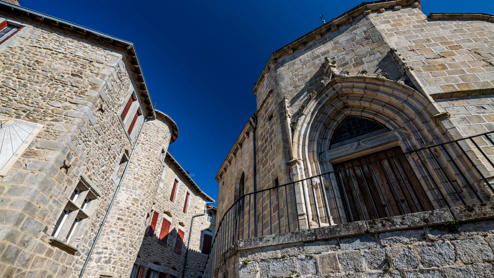 Vue de bas de l'entrée de l'église d'Olliergues et d'une maison de caractère jouxtant l'église
