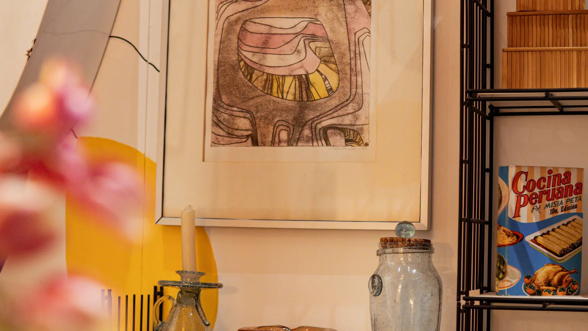 Une œuvre abstraite encadrée anime un espace où se mêlent verrerie, objets rétro et touches de couleur.