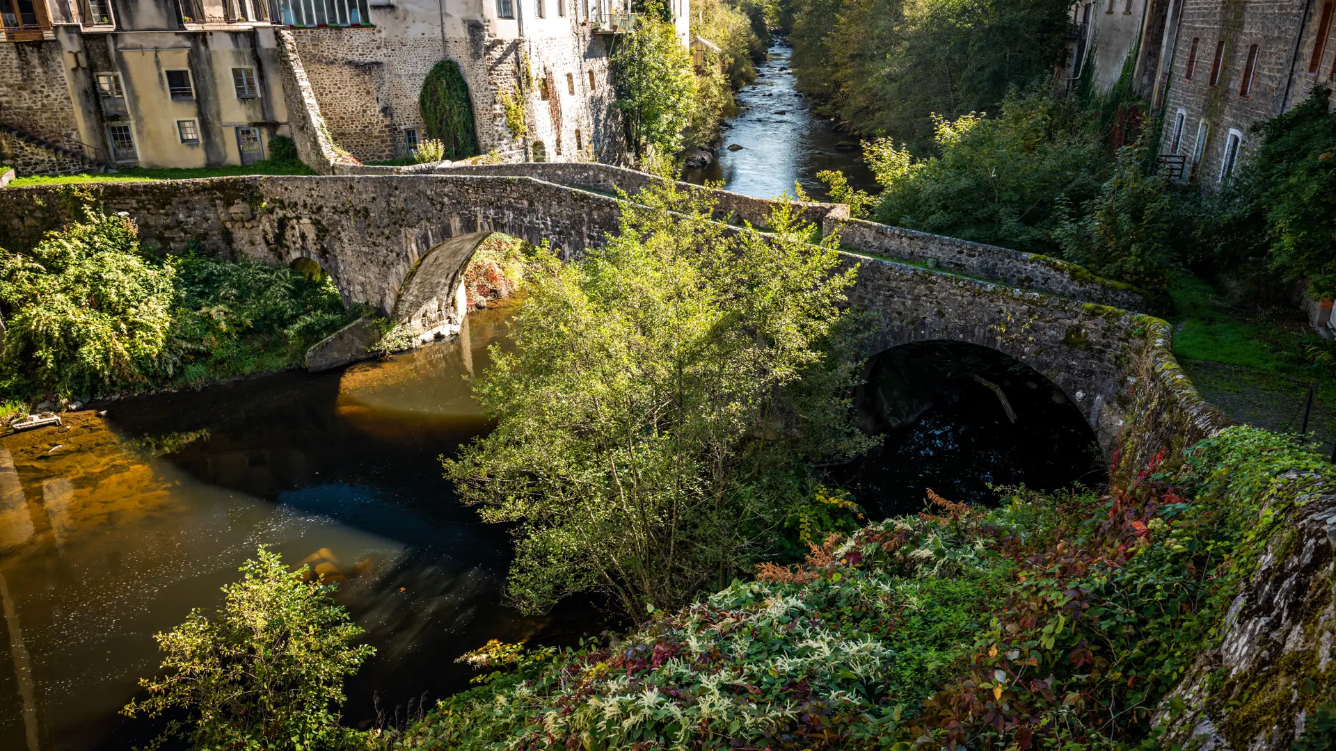 Un pont en pierre enjambe la Dore, la rivière qui parcours le bourg d'Olliergues dans un écrin de verdure