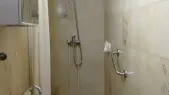 Cette salle d'eau fonctionnelle dispose d'une douche équipée d'une barre d'appui, d'un lavabo et d'un miroir, le tout revêtu de carrelage.