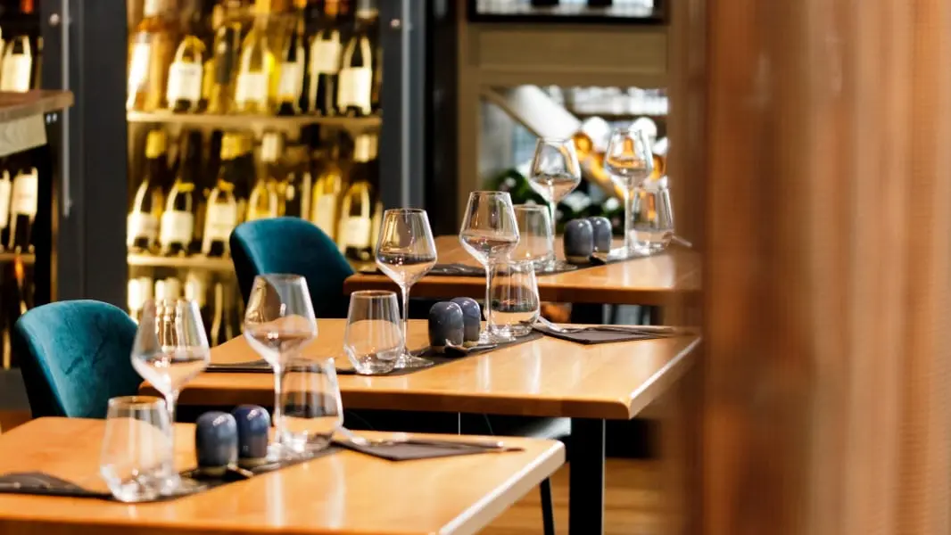 Le restaurant est décoré avec des tons chauds et naturels. Des tables dressées sont disposées dans la salle, et un grand mur de bouteilles de vin crée une ambiance conviviale.