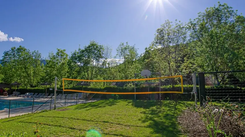 Le terrain de volley-ball est situé dans un environnement naturel, bordé d'arbres et à proximité d’une piscine.