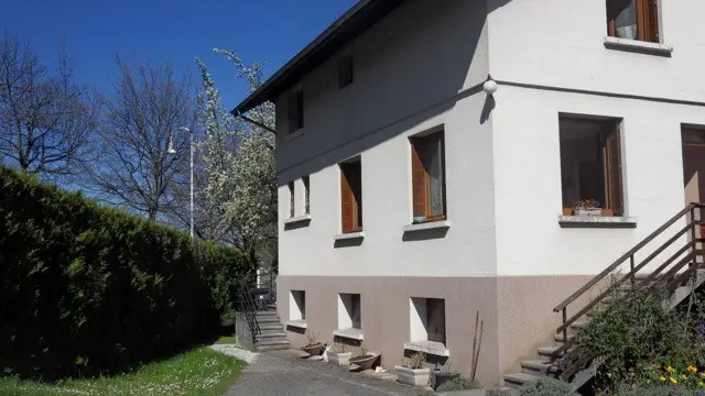 Cette maison individuelle, de construction traditionnelle, possède un étage et est dotée de fenêtres à volets en bois.