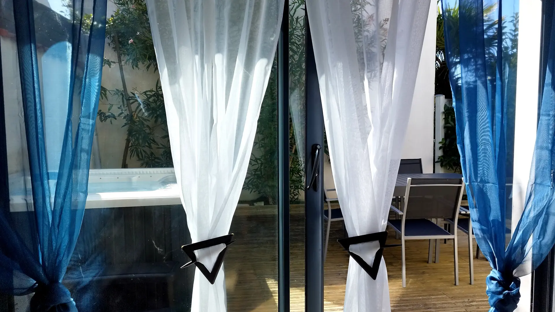 Porte-fenêtre avec rideaux donnant sur la terrasse et le jaccuzi.